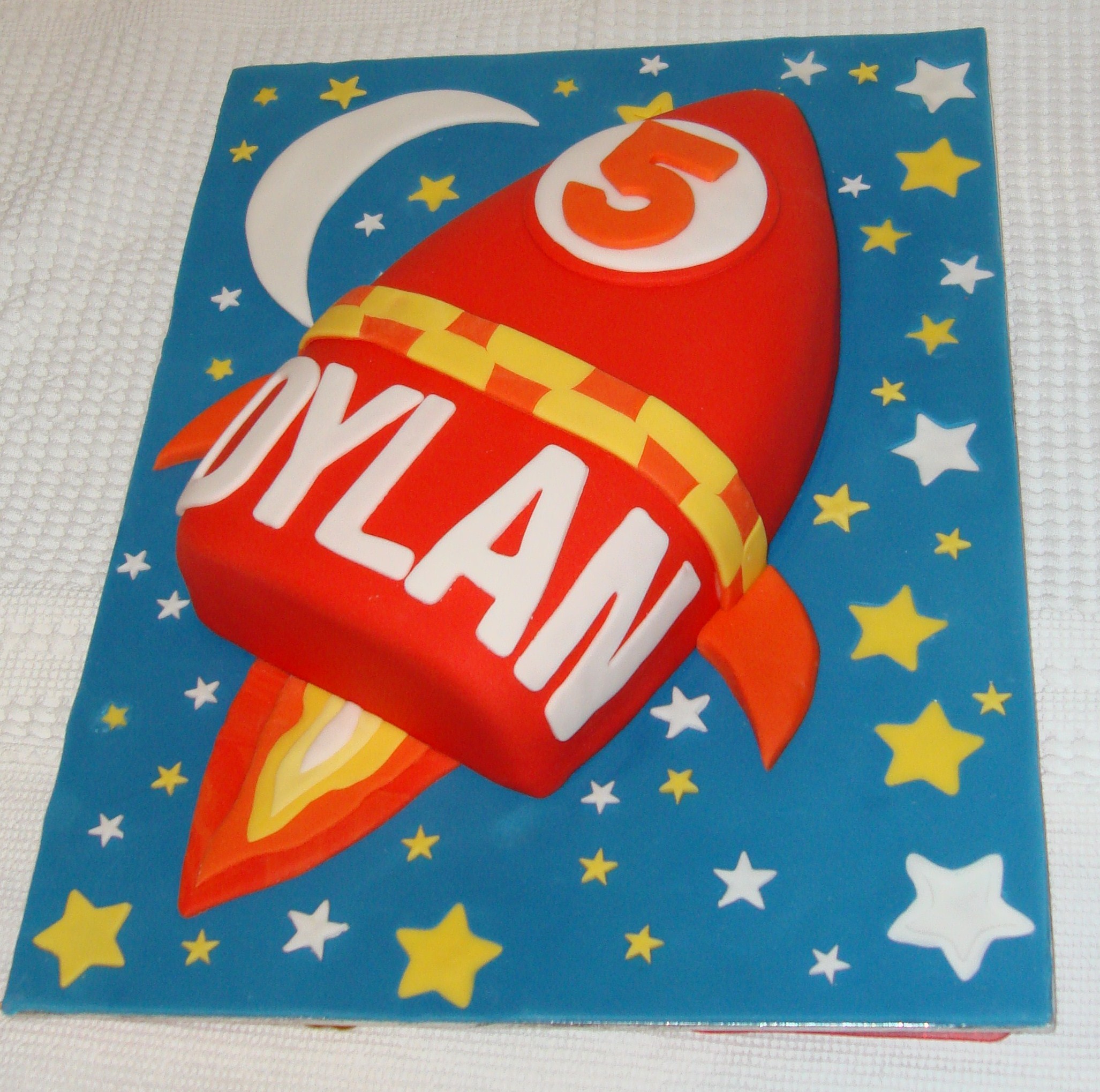 Fun kids birthday cake in the shape of a rocket that has stars in the background that lights up 