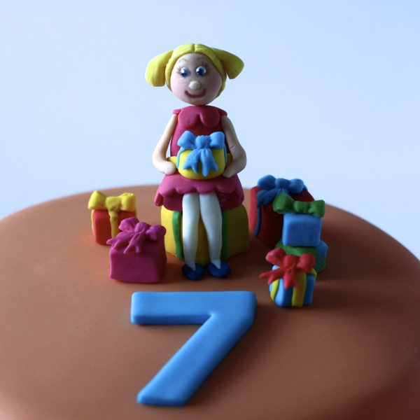 Bright birthday cake with girl sitting on the top and the name Amelia on the side